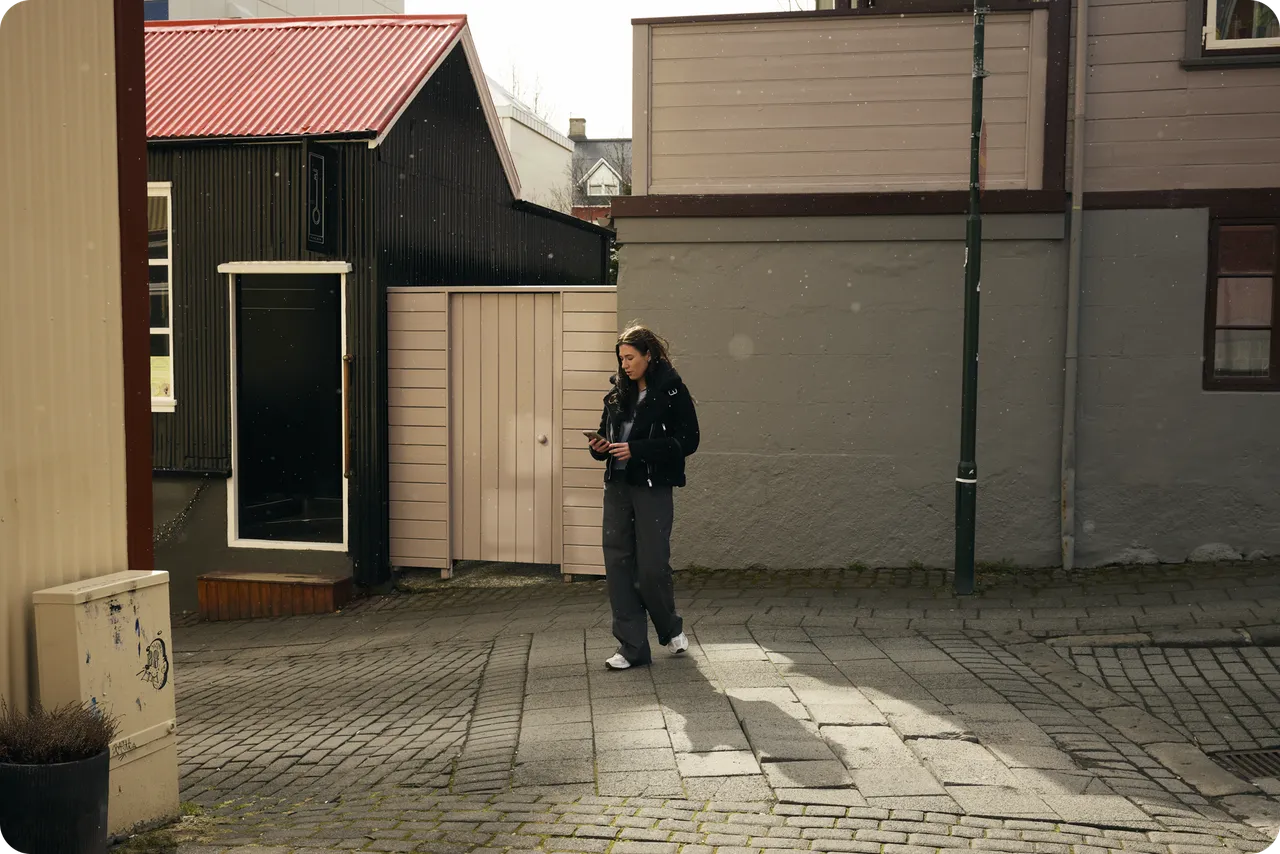 Einstaklingur gengur eftir hellulagðri götu og horfir á símann